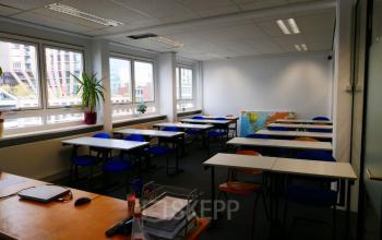 Office space for rent at Wijnhaven 76, Rotterdam Center, featuring multiple desks and chairs arranged in a spacious setting with large windows.