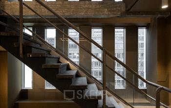 Interior view of a modern office at Stadhuisplein 9-23, Rotterdam Center, featuring industrial-style staircases and windowed walls. Ideal for office space rental.
