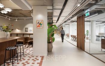 Modern office space at Stadhuisplein 9-23, Rotterdam Center with a sleek design, featuring a mix of wooden furniture and contemporary decor. A person is walking through the hallway.