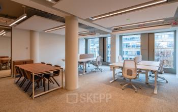 Modern office space for rent at Stadhuisplein 9-23, Rotterdam Center, featuring multiple desks and chairs under bright lighting with a view of city buildings.