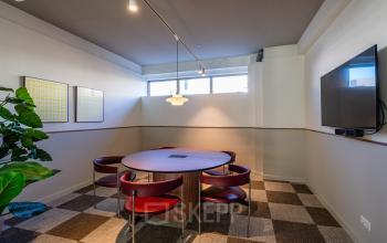 Cozy conference room with a round table, red chairs, wall art, and a large screen at Stadhuisplein 9-23 in Rotterdam Center, ideal for office space rental.