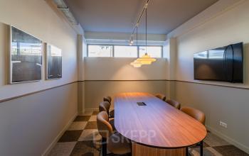 Rent office space in Rotterdam Center with a well-lit conference room featuring a wooden table, cushioned chairs, and a wall-mounted TV at Stadhuisplein 9-23.