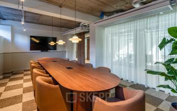 Modern conference room with a long wooden table, cushioned chairs, and a mounted TV at the office space rental in Rotterdam Center.