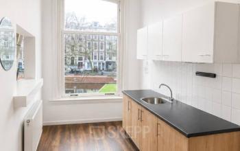 Bright, unfurnished office space at Mauritsweg 33 A01 in Rotterdam Center with hardwood floors, a large window, and a kitchenette, ideal for startups seeking office space rental.