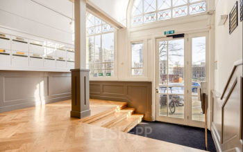 Bright entrance area of office space rental at Veerhaven 7, Rotterdam Center, featuring wooden flooring and tall windows letting in natural light.
