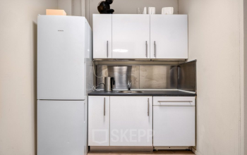 Compact kitchenette in an office space rental at Veerhaven 7, in Rotterdam Center, featuring white cabinets and a sleek counter.