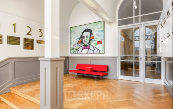 A stylish reception area at Veerhaven 7, Rotterdam Center, featuring parquet flooring, a vibrant painting, and a sleek red bench. Ideal space to rent as office or for office space rental.