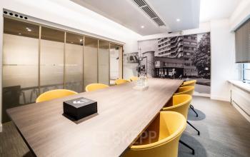 Modern conference room at Coolsingel 104, Rotterdam Center, featuring a long wooden table, bright yellow chairs, and wall decor of vintage Rotterdam imagery. Ideal office space rental for meetings.