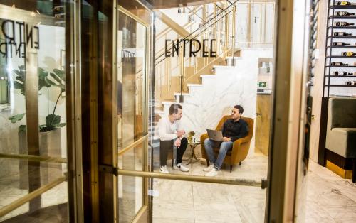 Modern office lounge at Coolsingel 104, Rotterdam Center with two people engaging in a business discussion near a staircase, featuring stylish furnishings and a contemporary design.