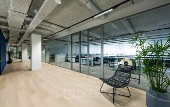 Modern office space at Westblaak 180, Rotterdam Center, with a glass-walled meeting room, sleek wooden flooring, and minimalistic furniture. Ideal for office space rental.