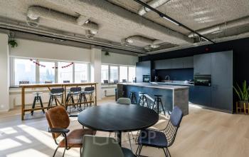 Bright office space rental at Westblaak 180, Rotterdam Center with modern furniture and a communal kitchen, perfect for coworking. Large windows provide natural light.