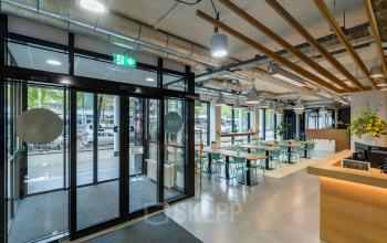 Modern office entrance at Westblaak 180 in Rotterdam Center, featuring bright lighting, open space with tables and chairs, and a view of the street through large windows.