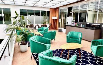 Modern lounge area with green chairs, wooden tables, and plants at an office to rent in Beursplein 37, Rotterdam Center.