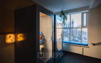 Office booths with a person working inside, located at Schiedamse Vest 154, Rotterdam Center; large window offering city view.