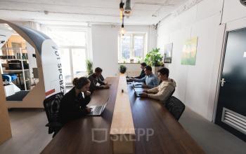 Office space rental located at Schiedamse Vest 154, Rotterdam Center, Rotterdam, featuring a modern workspace with individuals working diligently on laptops around a wooden table.