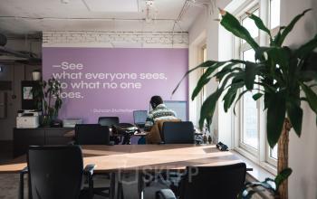 Modern office space rental at Schiedamse Vest 154, Rotterdam Center, featuring a large desk area with multiple chairs, potted plant, and an inspiring quote wall.