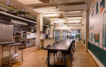 Spacious office space for rent at Kratonkade 7 - 27, Rotterdam Delfshaven, featuring a large communal table and kitchenette under festive lights.