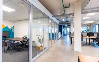 Modern office space at Kratonkade 7-27, featuring clear partitions, lounge chairs, and workstations, ideal for office space rental in Rotterdam Delfshaven.