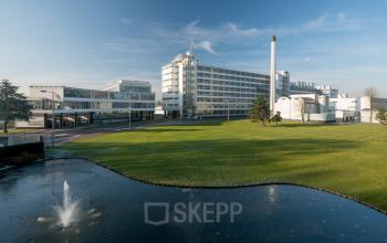 Exterior view of Van Nelleweg 1 in Rotterdam Delfshaven, an inviting location for office space rental, featuring a spacious landscape with a fountain.