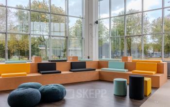 Bright, modern office space with colorful seating and large windows at Van Nelleweg 1 in Rotterdam Delfshaven available for rent.