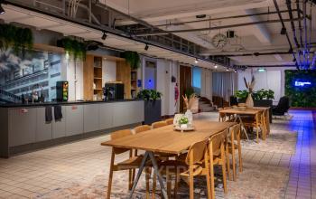 Spacious office interior at Van Nelleweg 1, Rotterdam Delfshaven, featuring modern wooden tables, chairs, and a coffee area for office space rental.