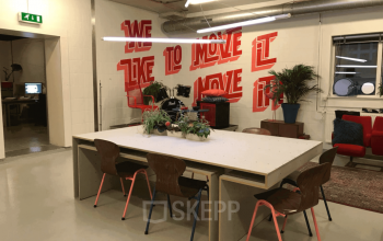 Interior view of a stylish office space with modern furnishings at Van Helmontstraat in Rotterdam Delfshaven, showing a large table with chairs, plants, and vibrant wall art.