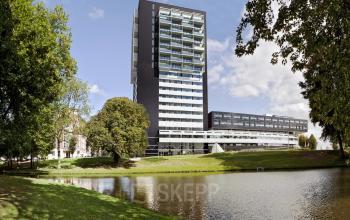 Exterior view of the modern office building at Westerlaan 10-65, Rotterdam Delfshaven, Rotterdam, situated beside a picturesque pond and surrounded by lush greenery.
