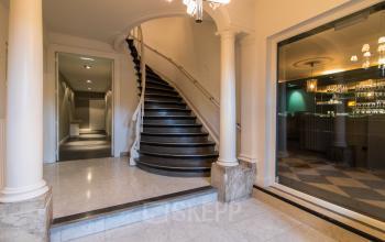 Interior of a Rotterdam office at Haringvliet 76 featuring a grand staircase with marble flooring and a glimpse of a dimly lit bar area, ideal for office space rental.