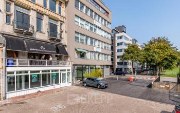 Exterior view of an office building at Haringvliet 76, Rotterdam. The facade features large windows and a secured parking area. Ideal location for office space rental.