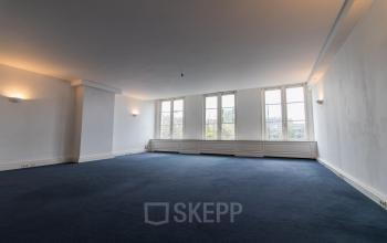 Spacious office to rent at Haringvliet 92, Rotterdam, featuring large windows allowing natural light and expansive carpeted area, perfect for customizing workspaces.