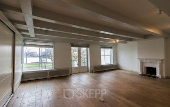 Spacious open floorplan with large windows providing natural light and scenic views at Haringvliet 92, Rotterdam. Ideal for office space rental, featuring wooden flooring and a decorative fireplace.