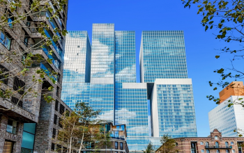 Exterior view of a modern office building located at Wilhelminakade 173, Rotterdam Kop van Zuid, ideal for office space rental with glass facade reflecting the blue sky.