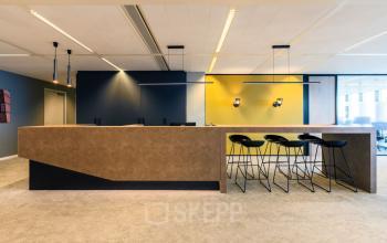 Modern office reception area in Rotterdam Kop van Zuid, located at Wilhelminakade 173, featuring a sleek reception desk with bar stools and contemporary lighting.