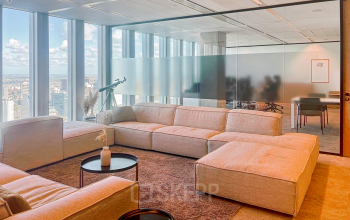 Spacious office lounge with comfortable seating and large windows offering a view of Rotterdam. Ideal for relaxing in a rented office space.