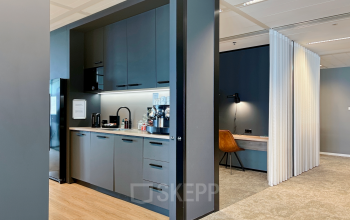 Modern office kitchen area with sleek cabinets and a coffee machine located in Rotterdam Kop van Zuid. Adjacent workspace for office space rental.