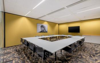 Modern conference room with U-shaped table setup, chairs, a wall-mounted TV, and vibrant yellow walls at Wilhelminakade 173 in Rotterdam Kop van Zuid, available for office space rental.
