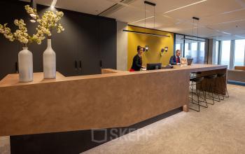 Modern reception area at Wilhelminakade 173, Rotterdam Kop van Zuid, featuring a wooden desk, chairs, and wall with yellow accents.
