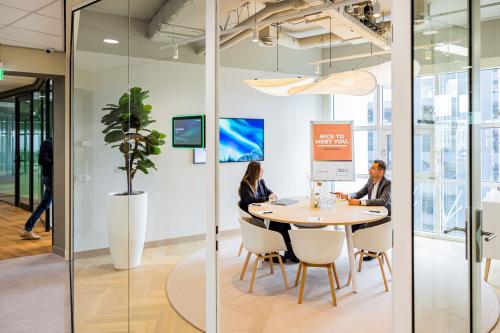 Modern office space for rent in Rotterdam's Kop van Zuid, featuring a stylish conference room with a round table, smart lighting, and large windows offering natural light. Ideal for meetings or collaborative work.