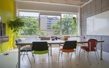 Bright conference room at Zomerhofstraat 71, Rotterdam North, featuring a large table with colorful chairs, window views, and greenery.
