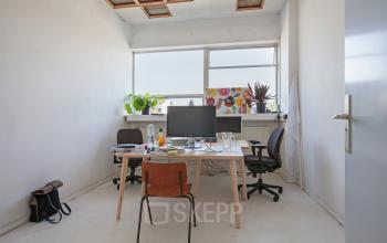 Modern office space rental at Zomerhofstraat 71, Rotterdam Noord, with a tidy desk, computer, and vibrant art.