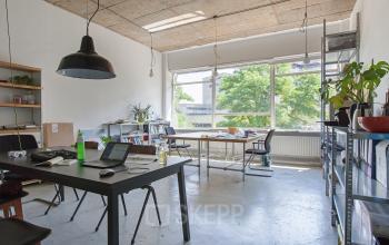 Office space for rent at Zomerhofstraat 71, Rotterdam North. The interior features tables, chairs, shelves, and large windows providing ample natural light.