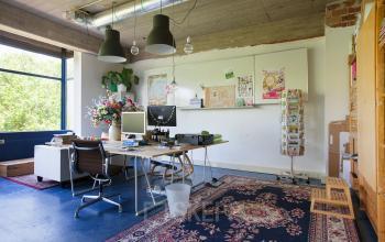 Bright office space with large window, colorful chairs, computer setup, whiteboard, and decorative plants located at Vijverhofstraat 47, Rotterdam North, available for office space rental.