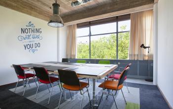 Conference room at Vijverhofstraat 47, Rotterdam North, featuring a modern table with colorful chairs, large windows with curtains, and a motivational wall quote.