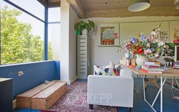 Casual office space with large windows, a white sofa, a desk with floral decor, and vibrant wall art at Vijverhofstraat 47, Rotterdam North.