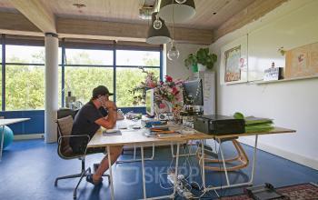 Office space in Vijverhofstraat 47, Rotterdam North, with large windows, a desk, office supplies, and a person working at a computer.
