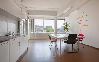 Bright office space rental in Rotterdam Noord with large windows, meeting table, chairs, and built-in kitchenette at Vijverhofstraat 47.
