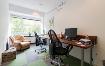 Furnished office space rental at Zomerhofstraat 84, Rotterdam North, featuring desks, chairs, computer monitors, and a casual seating area with a sofa and natural light from the window.