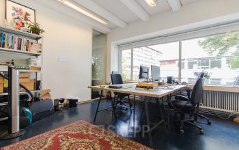 Bright office space with large windows, shelves with books, desks with chairs, and computer monitors at Zomerhofstraat 84, Rotterdam. Ideal for office space rental.