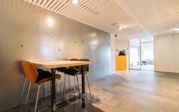 Interior view of office space at Zomerhofstraat 84, Rotterdam North, with a high table and chairs near a gray wall, leading to a furnished area.