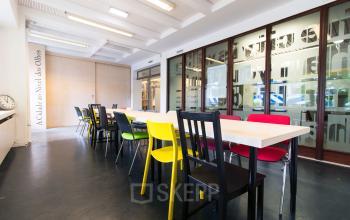 Office space rental at Zomerhofstraat 84 in Rotterdam North featuring a long table with multicolored chairs in a light and spacious interior.